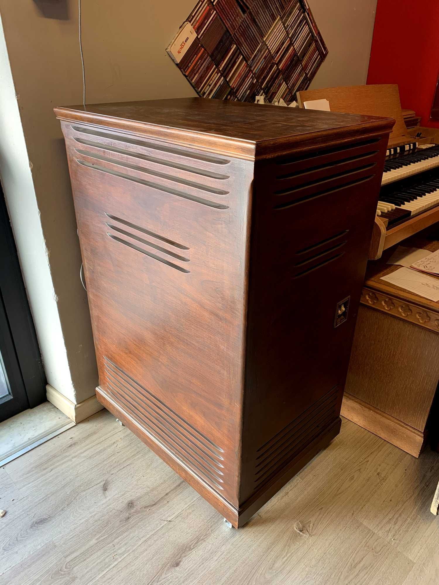 Wooden, rectangular speaker cabinet with horizontal vents, next to a window and organ.