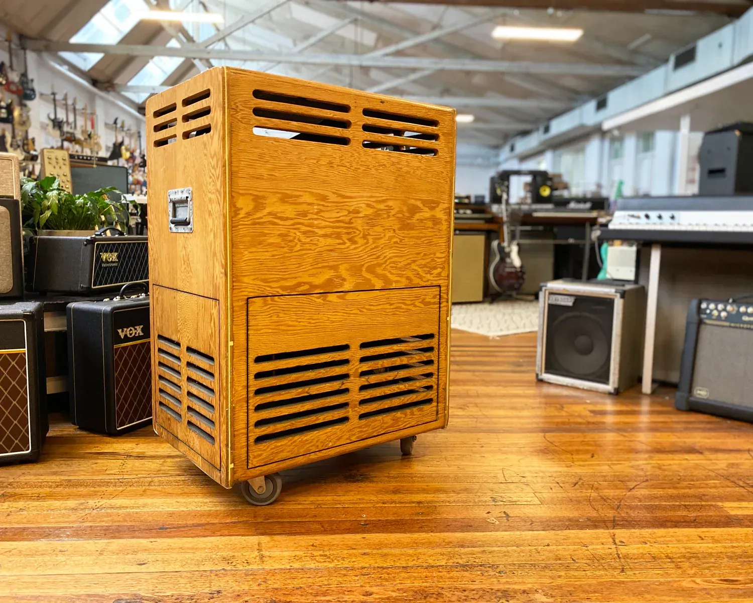 Large, wooden amplifier cabinet on wheels with ventilation slots, in a music store.