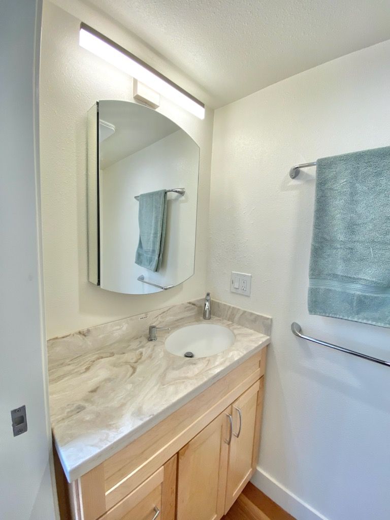 Bathroom with light-colored vanity, oval sink, and a curved mirror. A teal towel hangs on the wall.