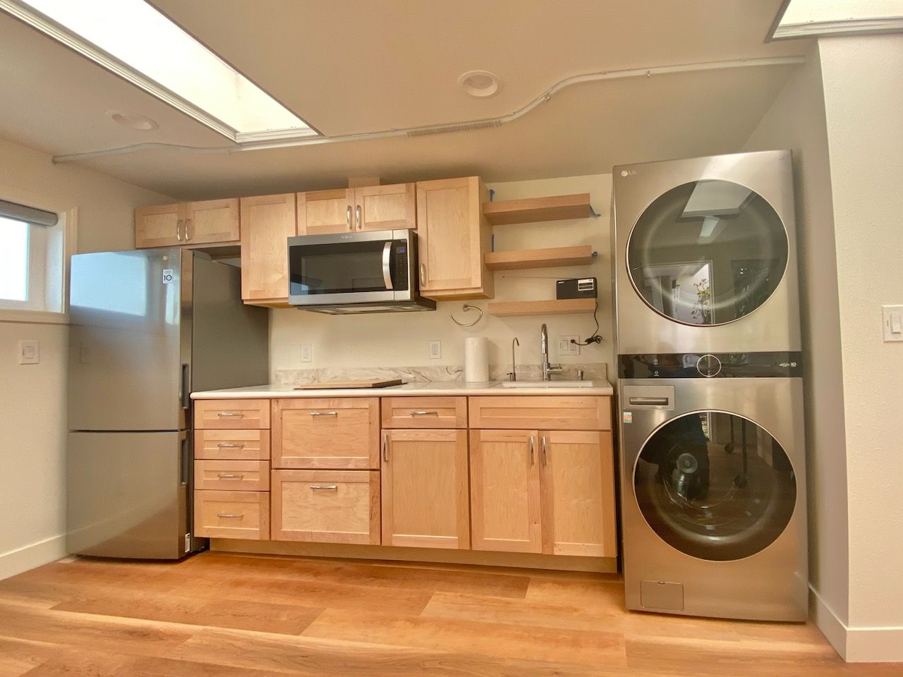 Kitchenette with light wood cabinets, stainless steel appliances, and stacked washer/dryer.