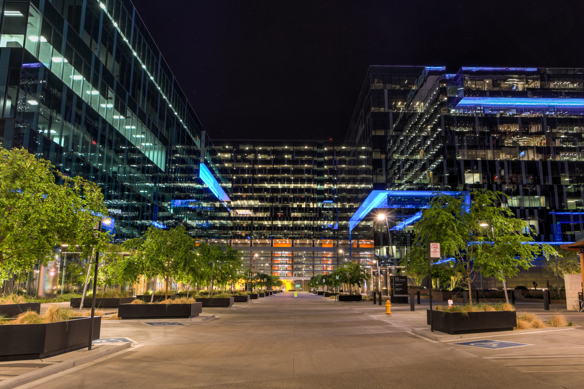 Night view of modern buildings, street with trees, and lights illuminating the cityscape.