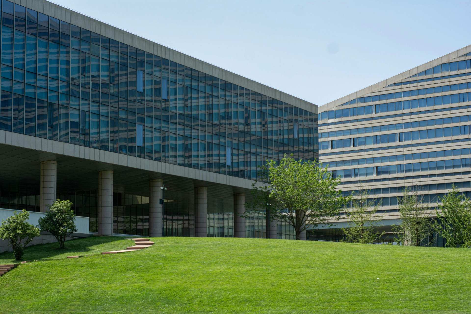 Modern glass and concrete buildings with grassy area, sunny day.