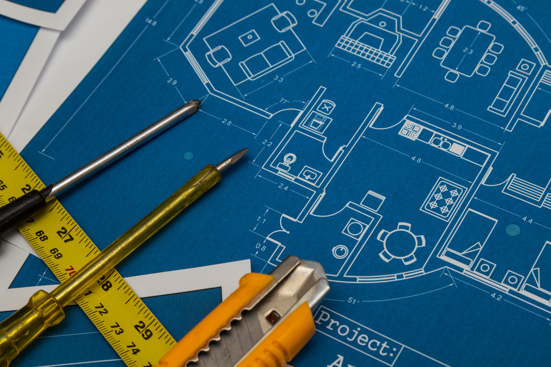 Blueprints with tools, including a ruler, screwdriver, and utility knife, representing architectural planning.