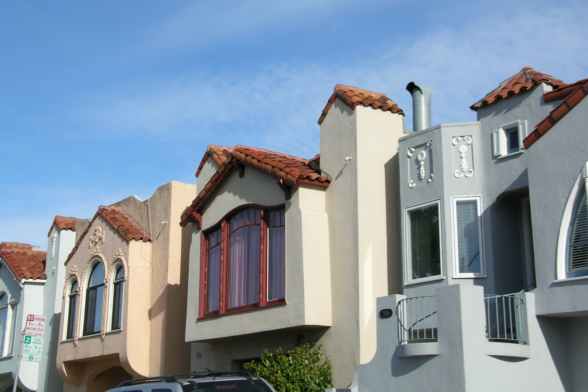 Row of colorful stucco houses with red tile roofs against a blue sky.