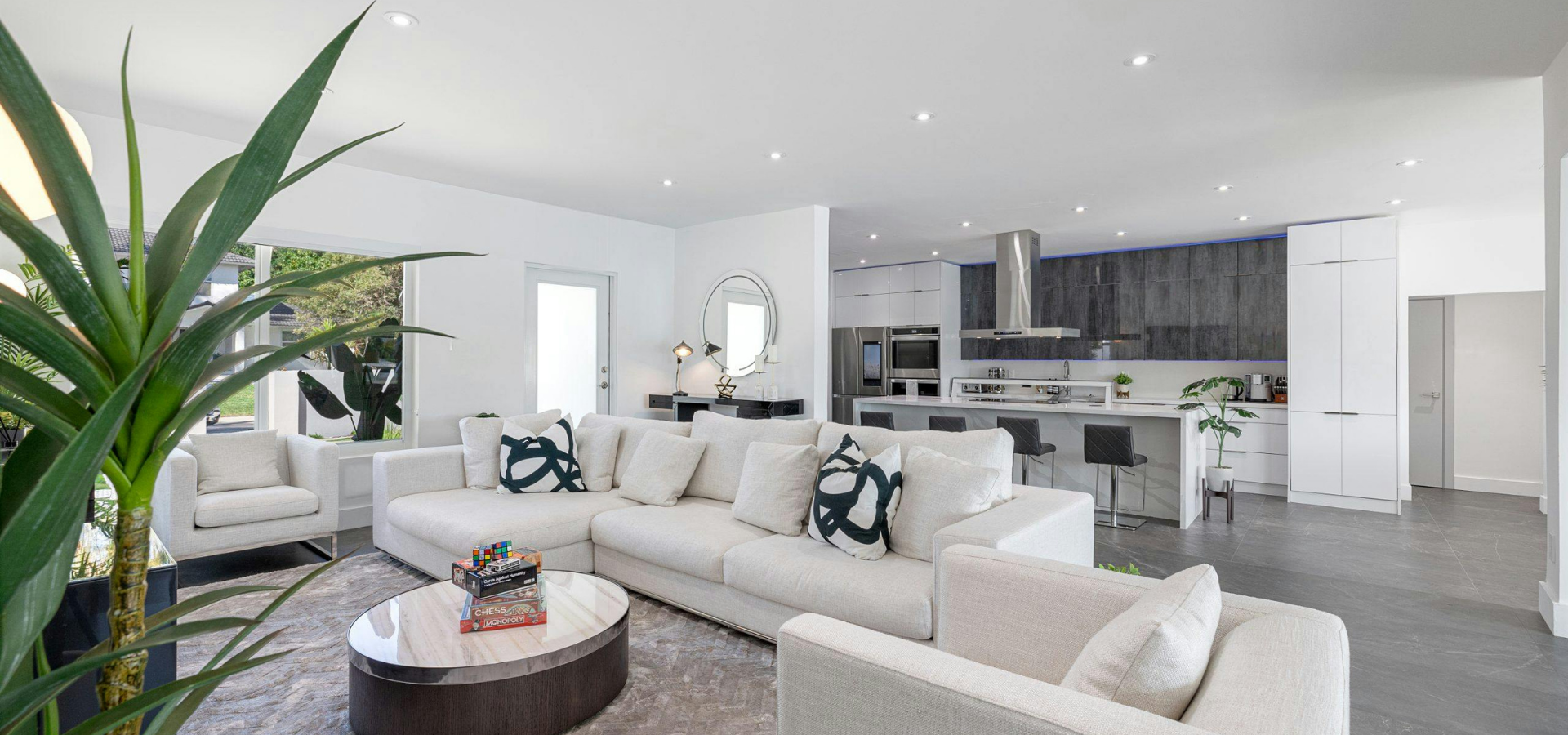 Bright modern living room with white sofas, round coffee table, and open kitchen in the background