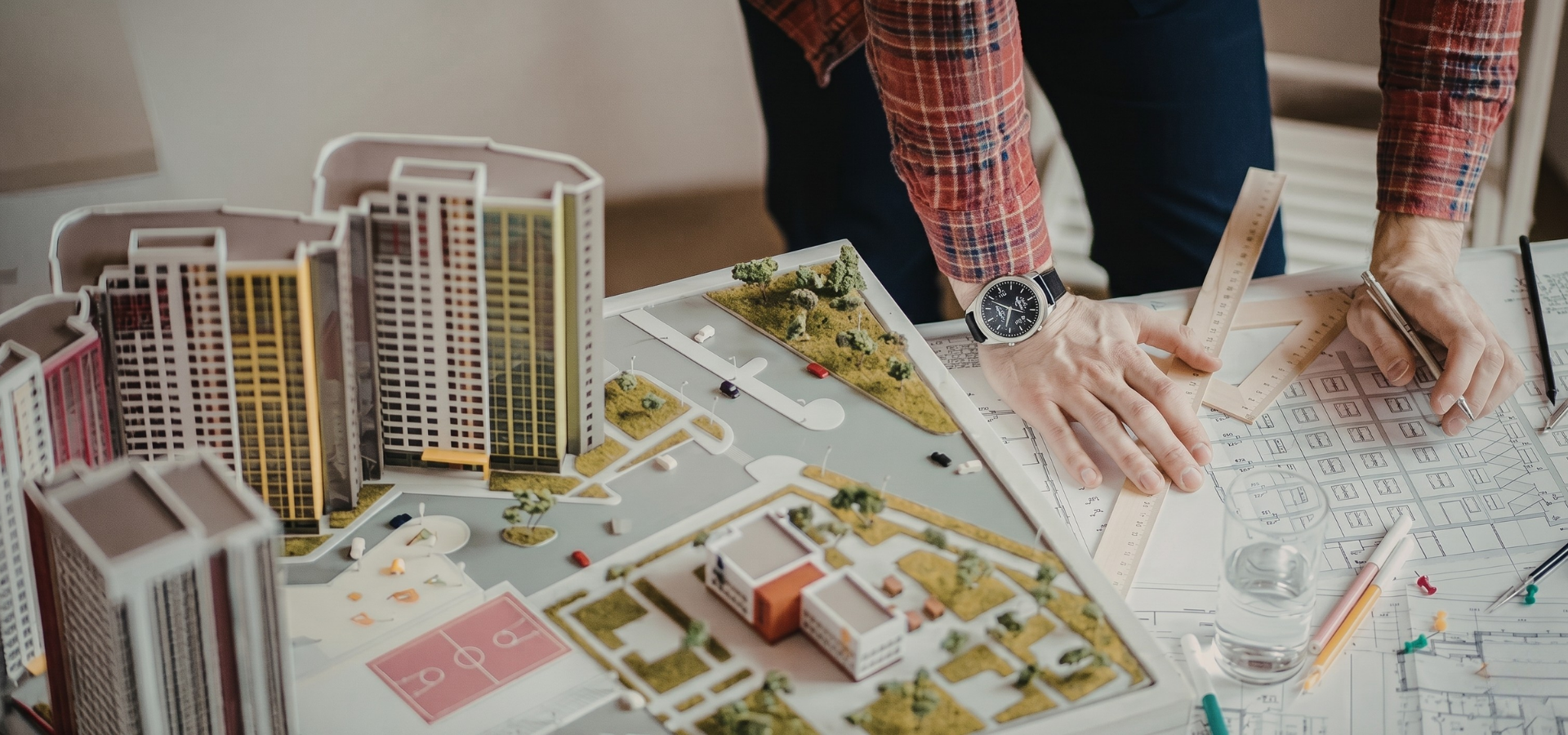 Hands reviewing a detailed architectural scale model with floor plans and high-rise buildings