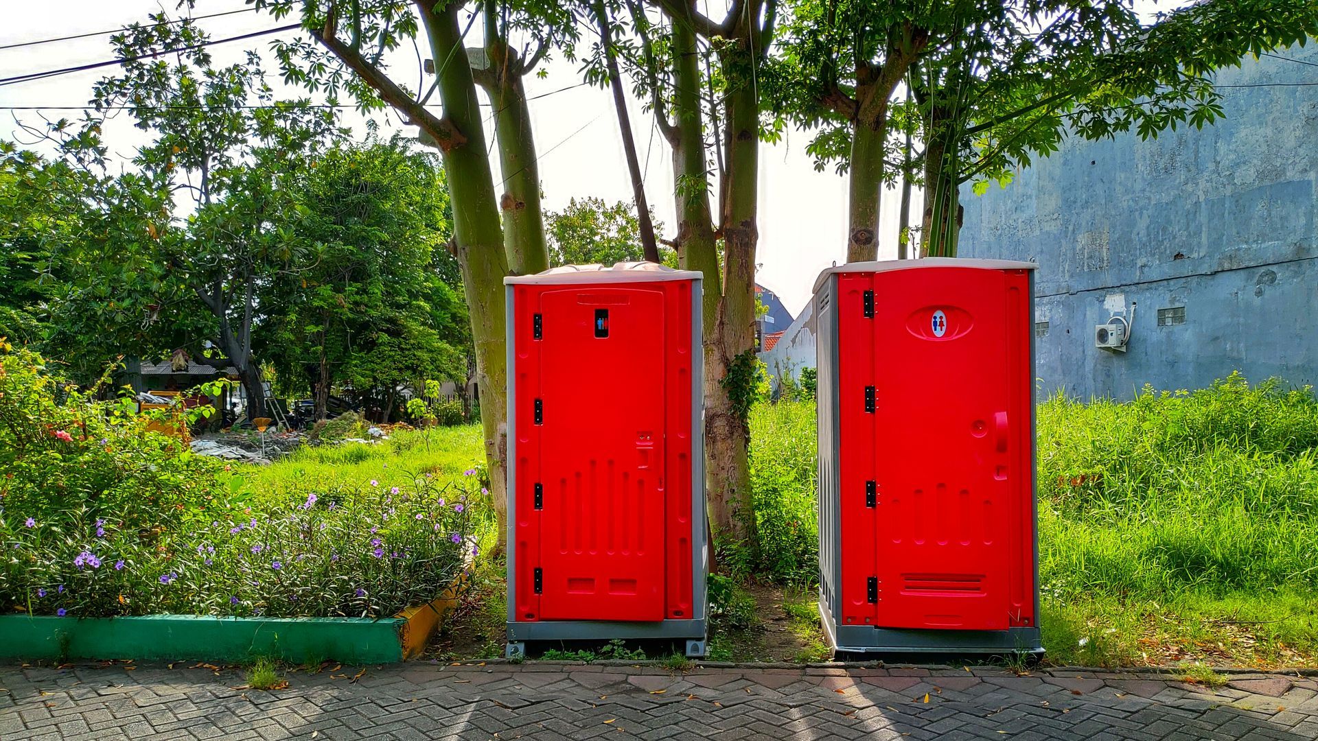 Red portable toilets on ground, with a forest background, representing portable toilets hires.