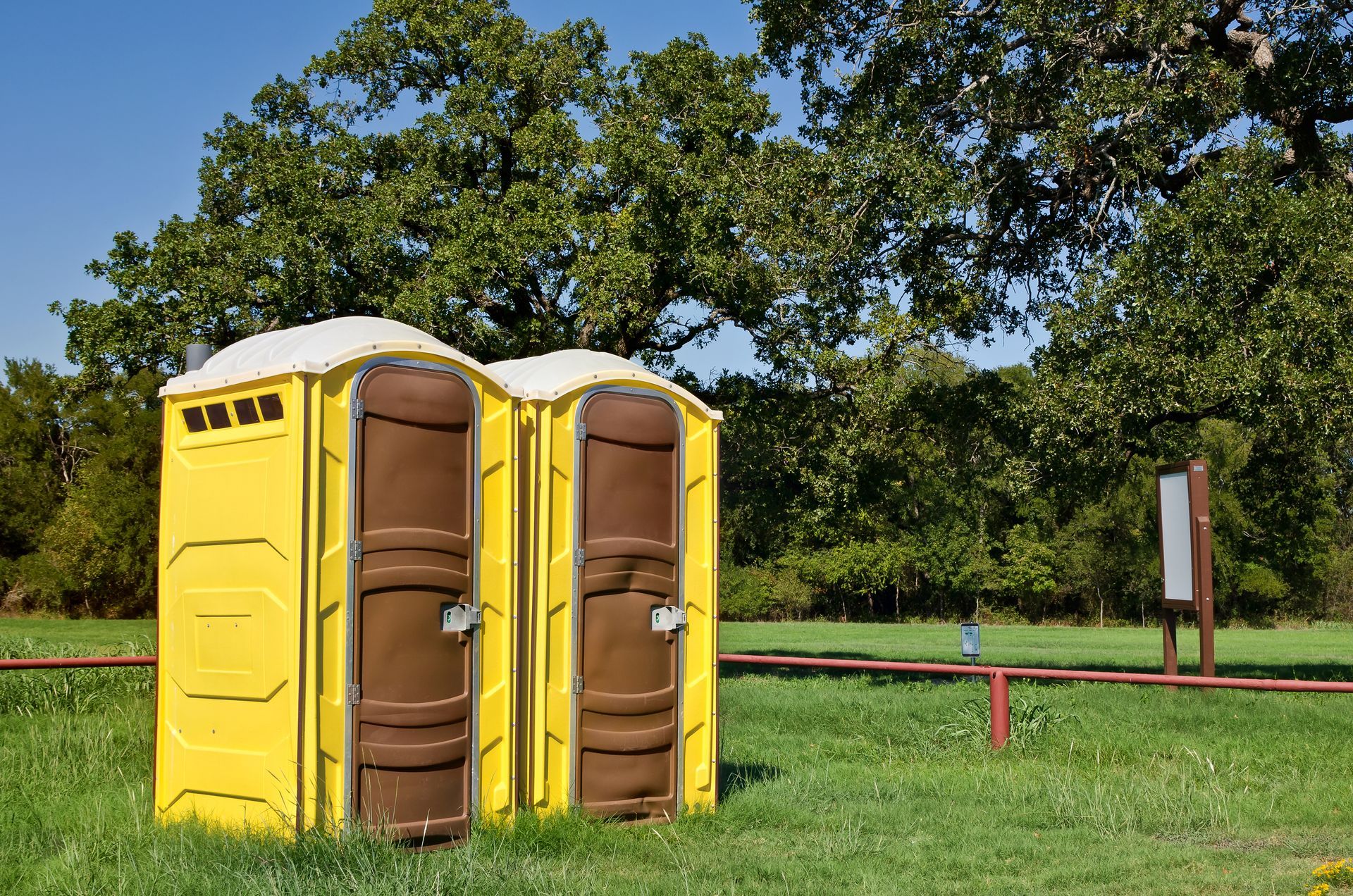 Yellow portable toilets are on ground with a park as background, representing portable toilet hires.