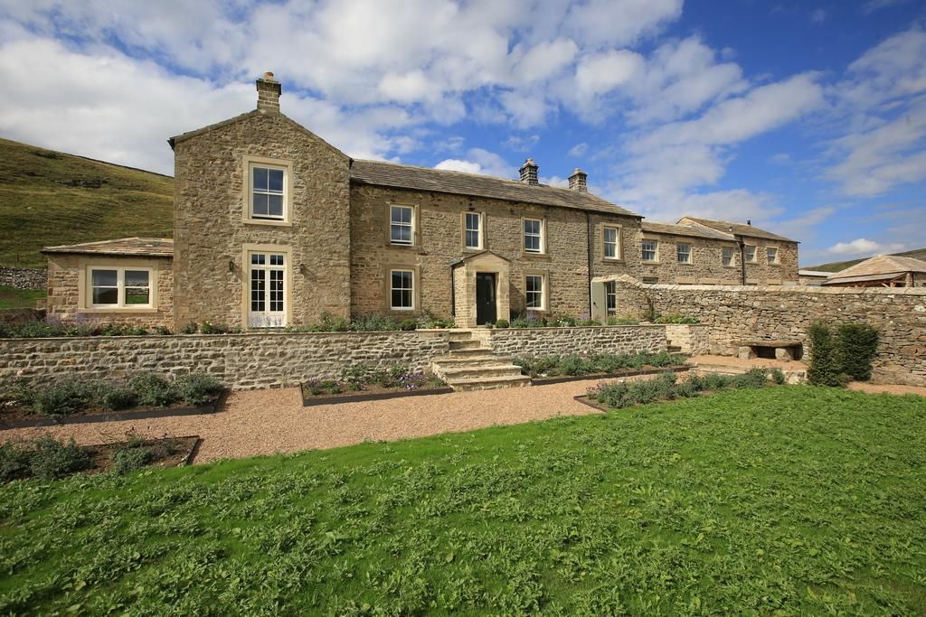 Stone house with a green lawn, flower beds, and a bright blue sky.