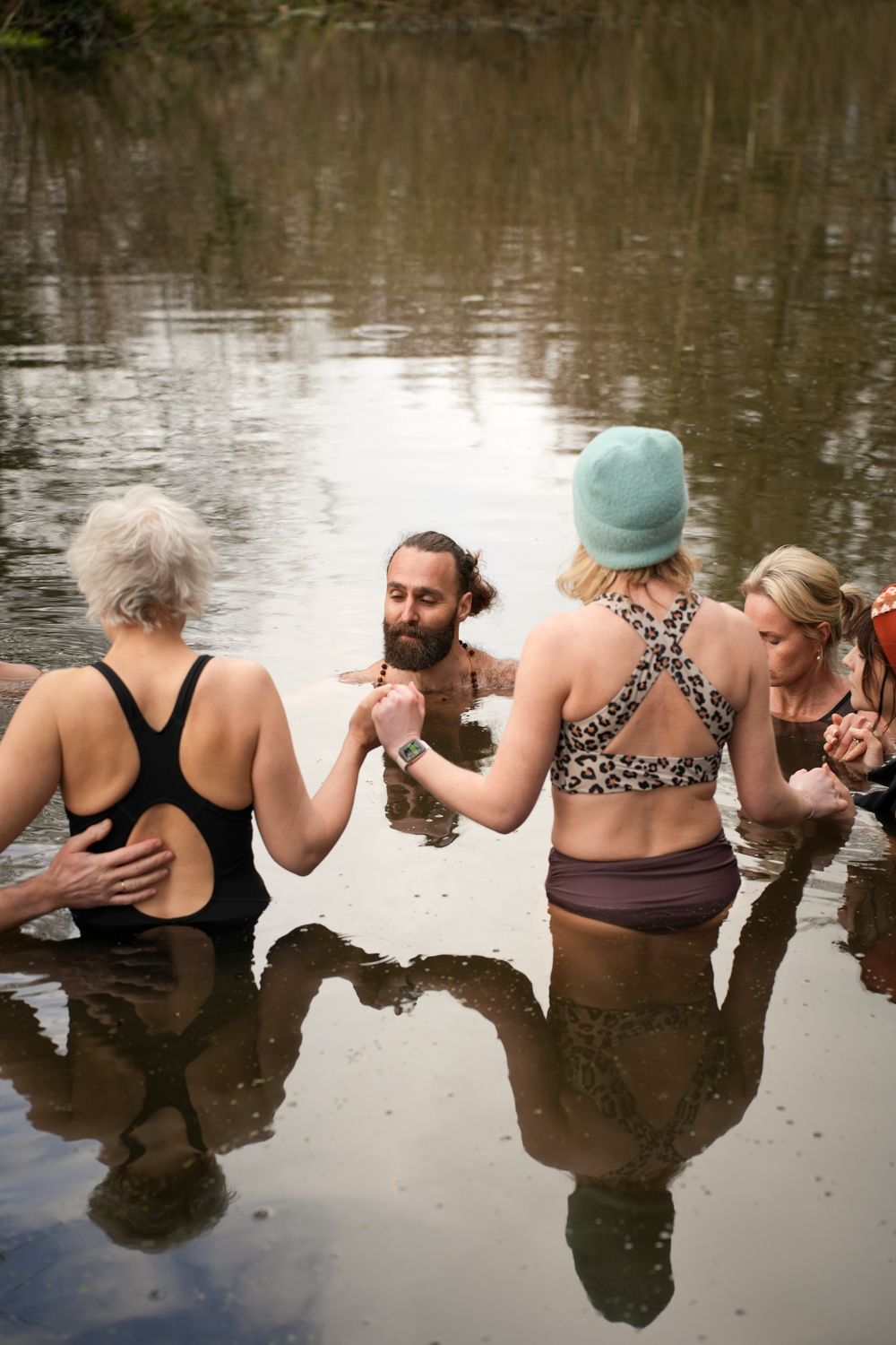 People stand in a circle holding hands in calm water, with reflections visible on the surface.