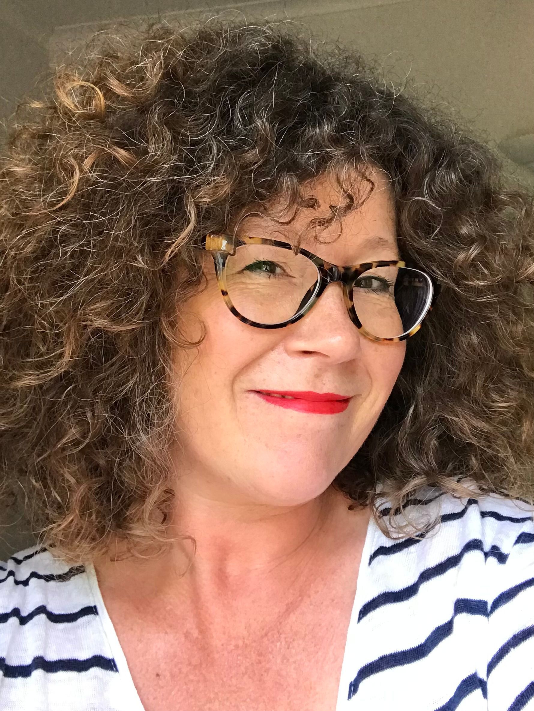 A woman wearing glasses and a white shirt is smiling for the camera.