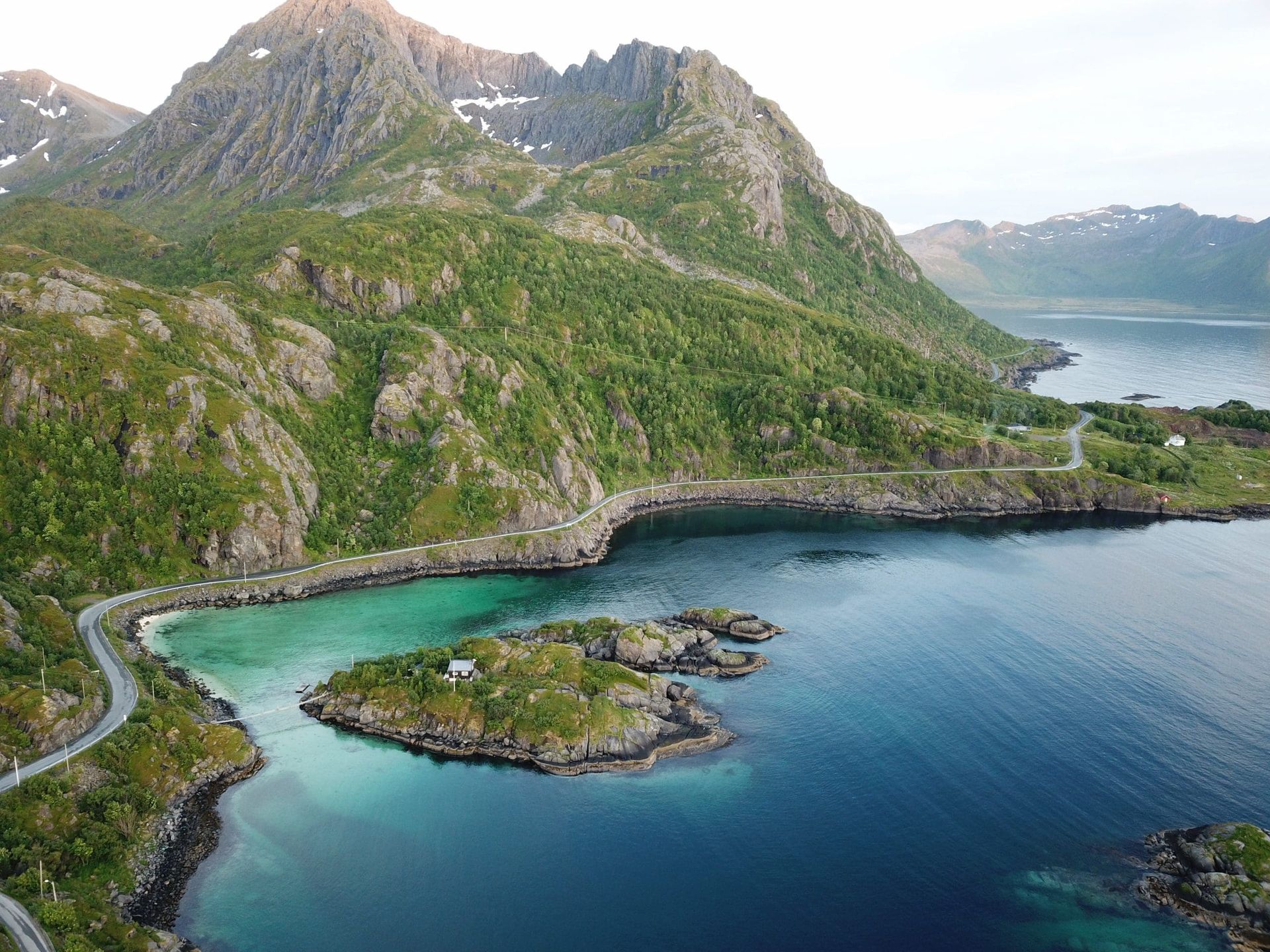 An aerial view of a small island in the middle of a large body of water surrounded by mountains.