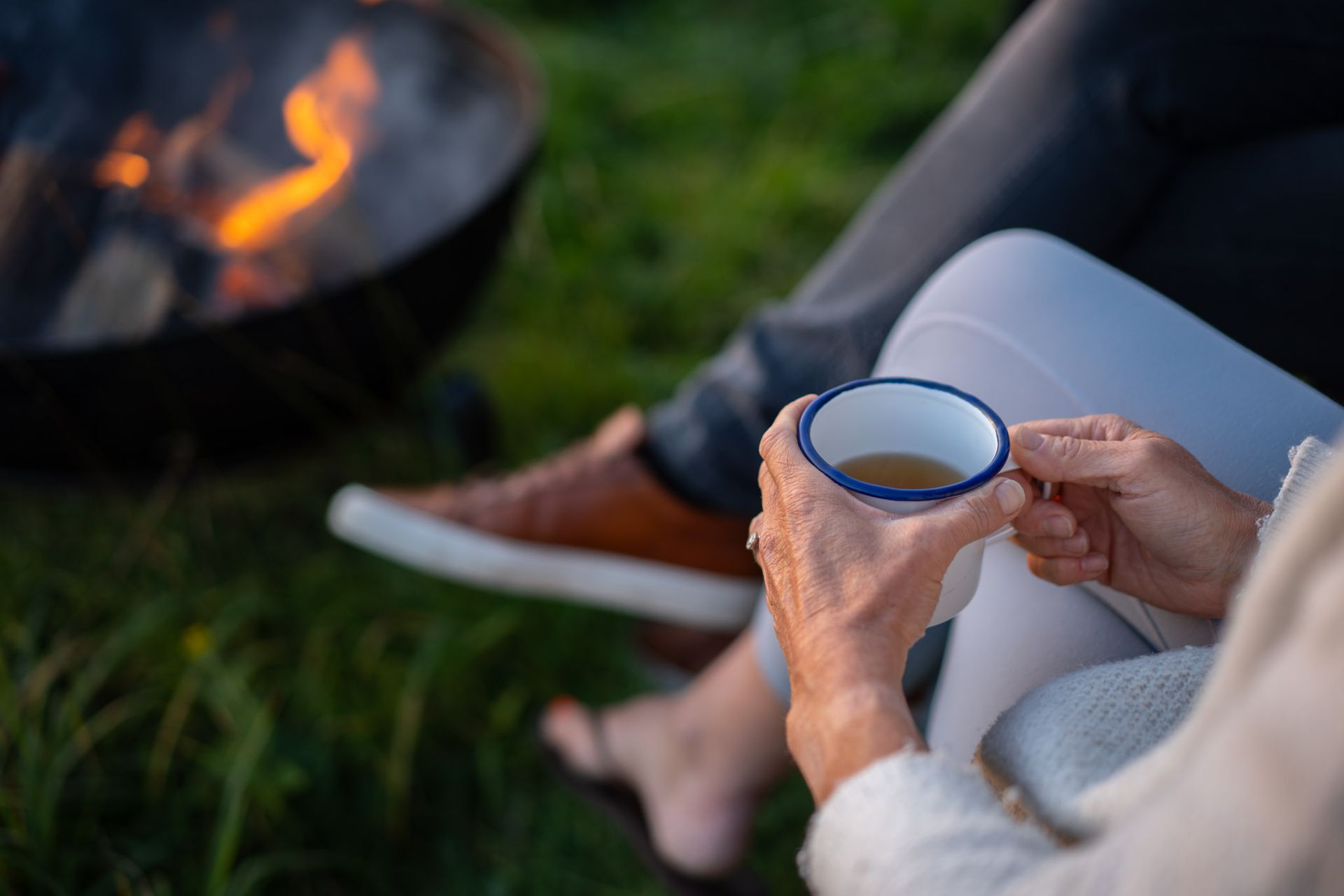 A woman is sitting in the grass holding a cup of tea.