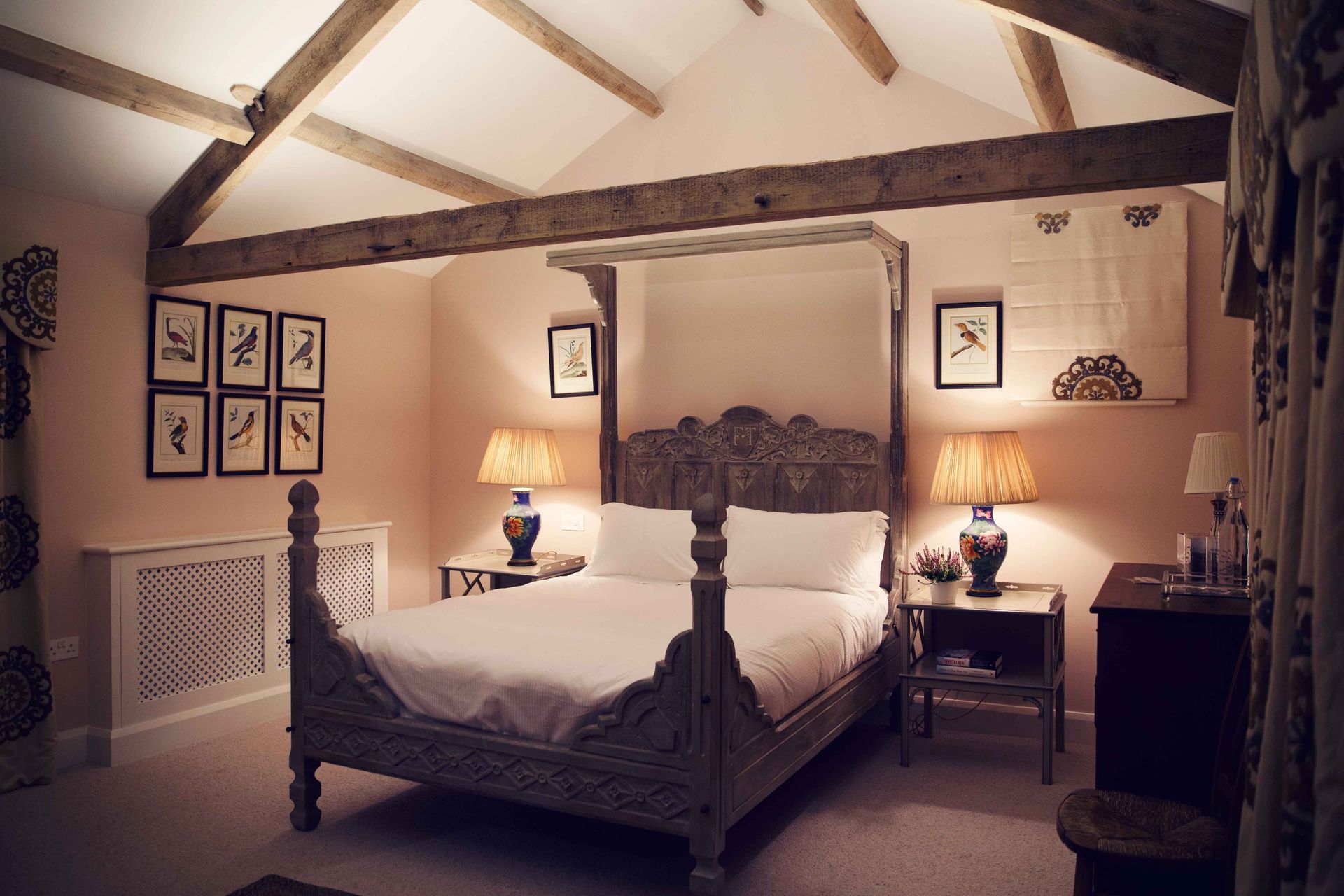Bedroom with a four-poster bed, wooden beams, and framed art on a pink wall.