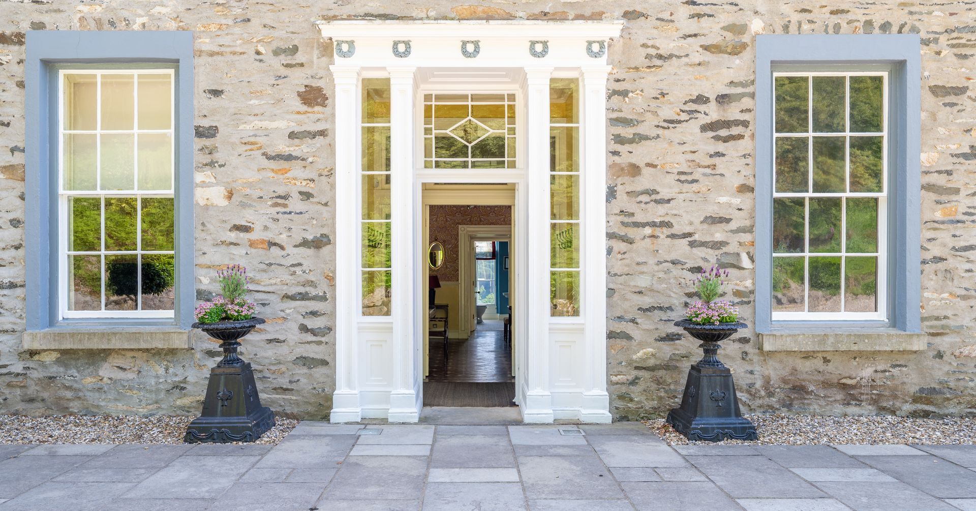 Stone facade with white doorway and windows, two black planters on stone patio.