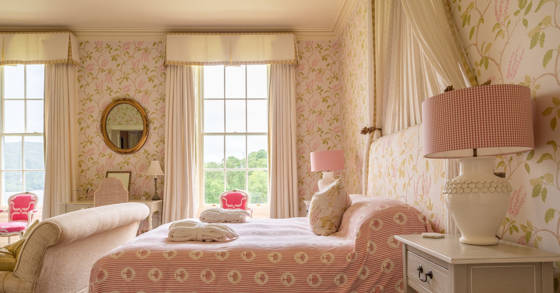 Pink floral bedroom with large windows, canopy bed, and antique furniture.