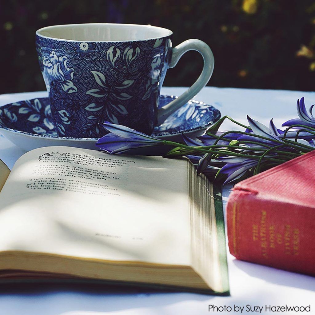 A cup of tea sits on a saucer next to an open book