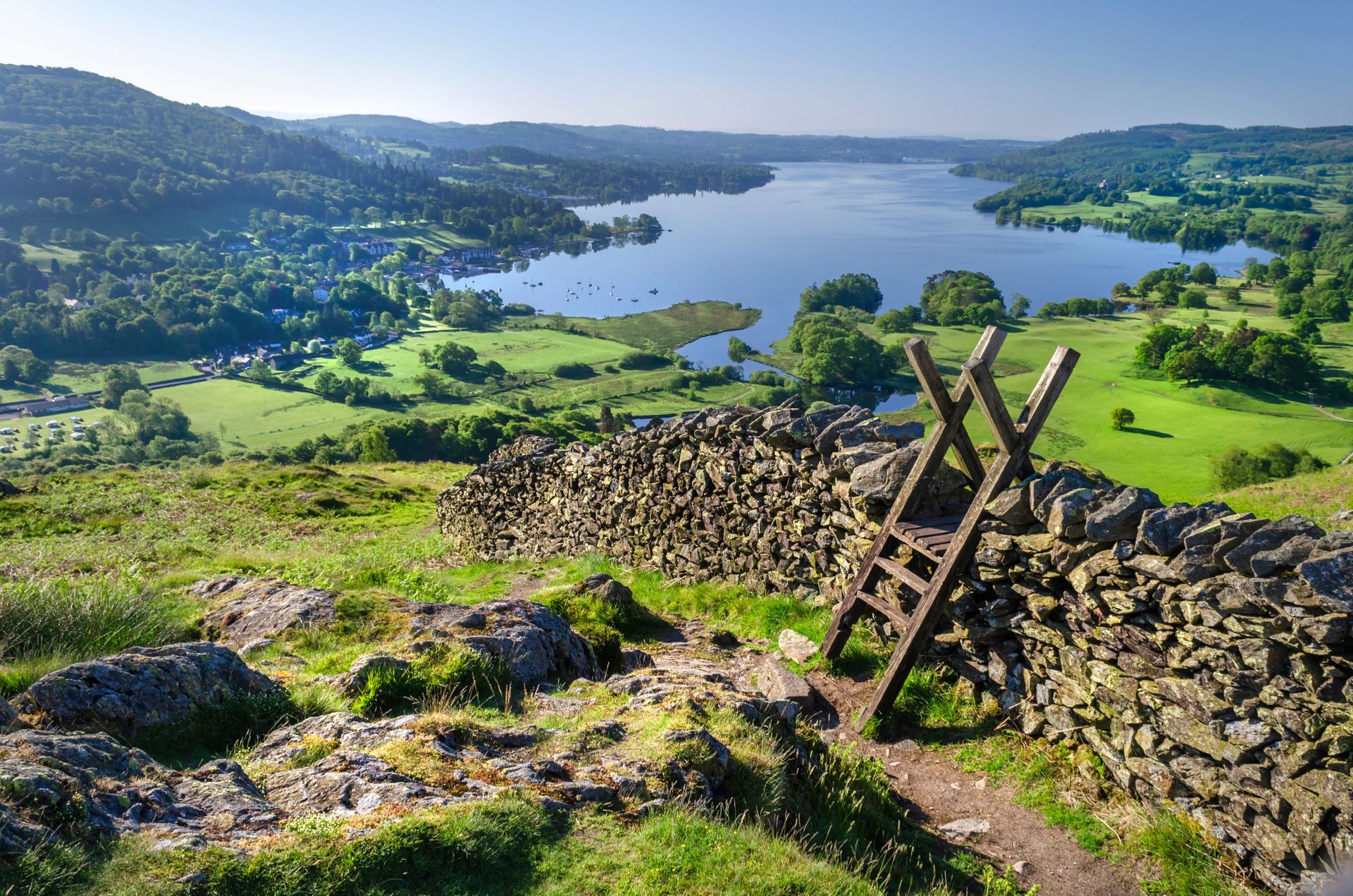 View of lake and green hills with stone wall and wooden stile in foreground.