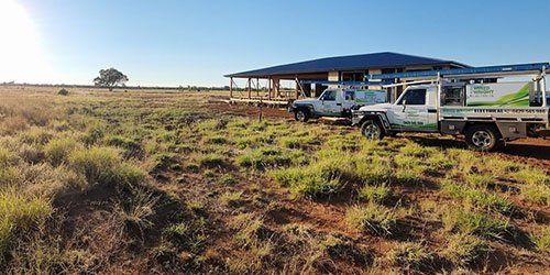 Two work utes are parked in a grassy field in front of a house.