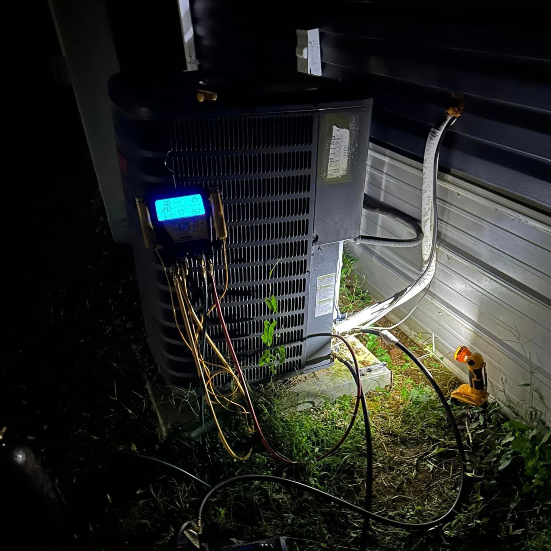 An air conditioner is being serviced by a technician at night.