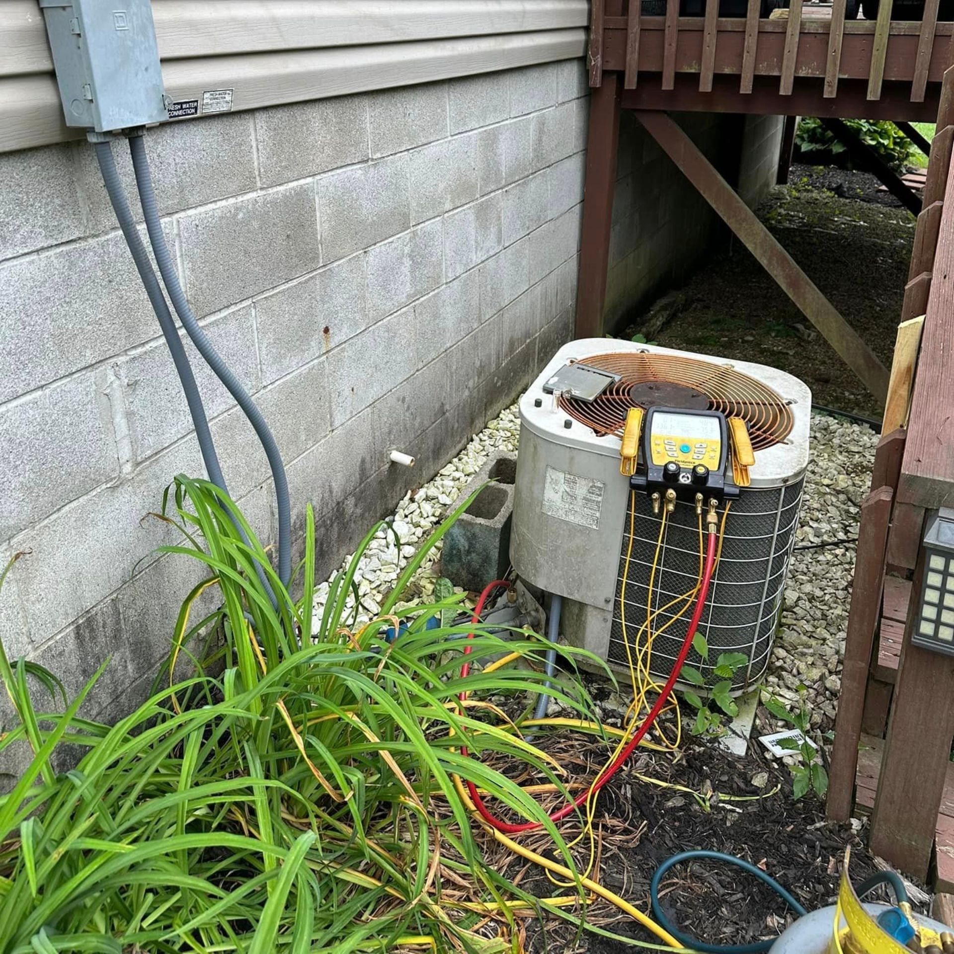 An air conditioner is being repaired outside of a house.