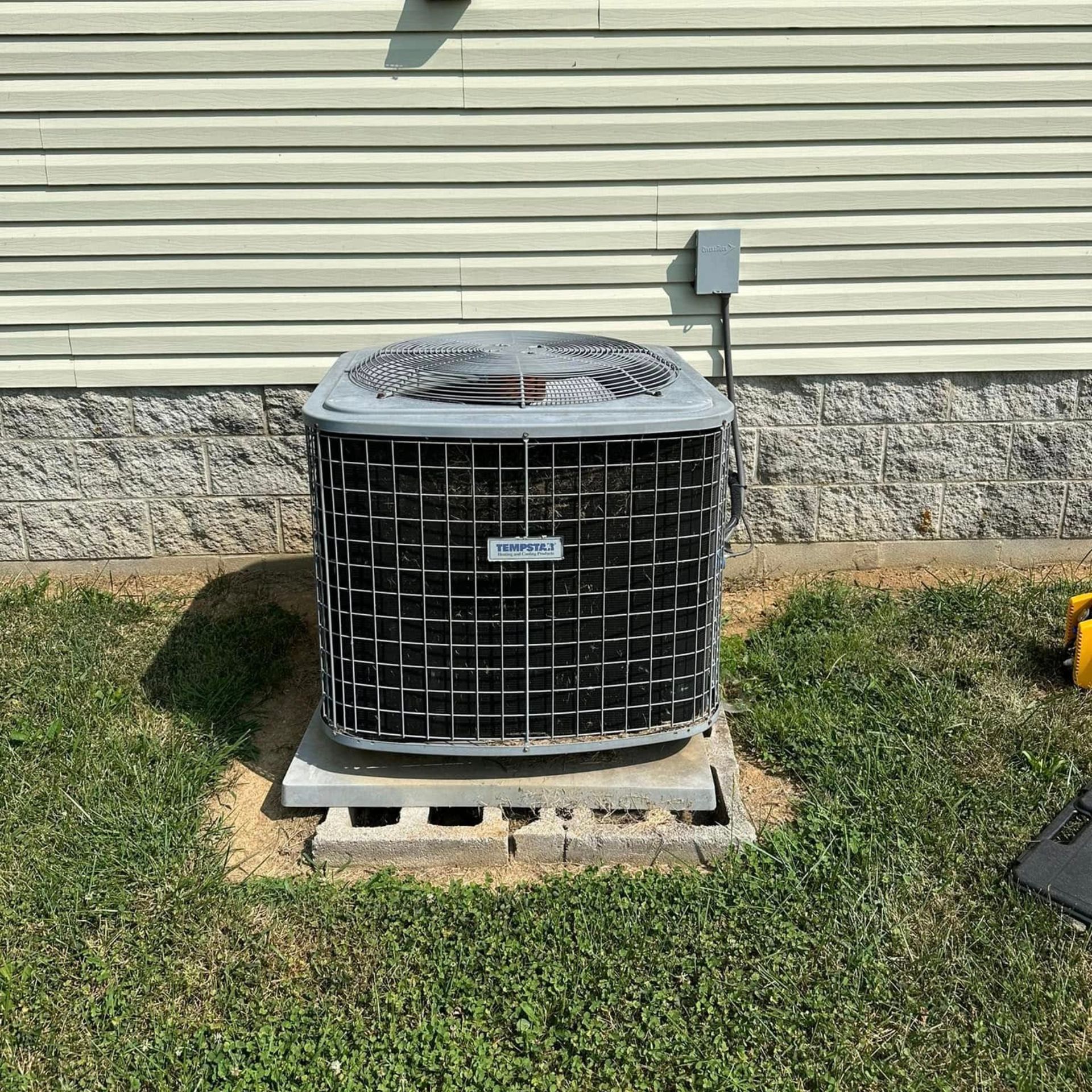 An air conditioner is sitting in the grass in front of a house.