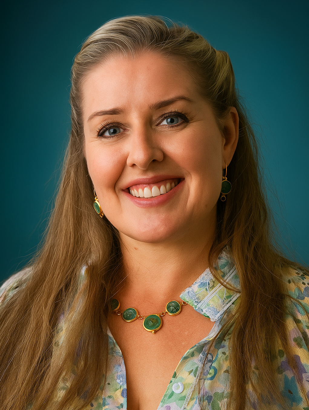 Woman with long hair smiles, wearing a floral shirt and green jewelry. Turquoise background.