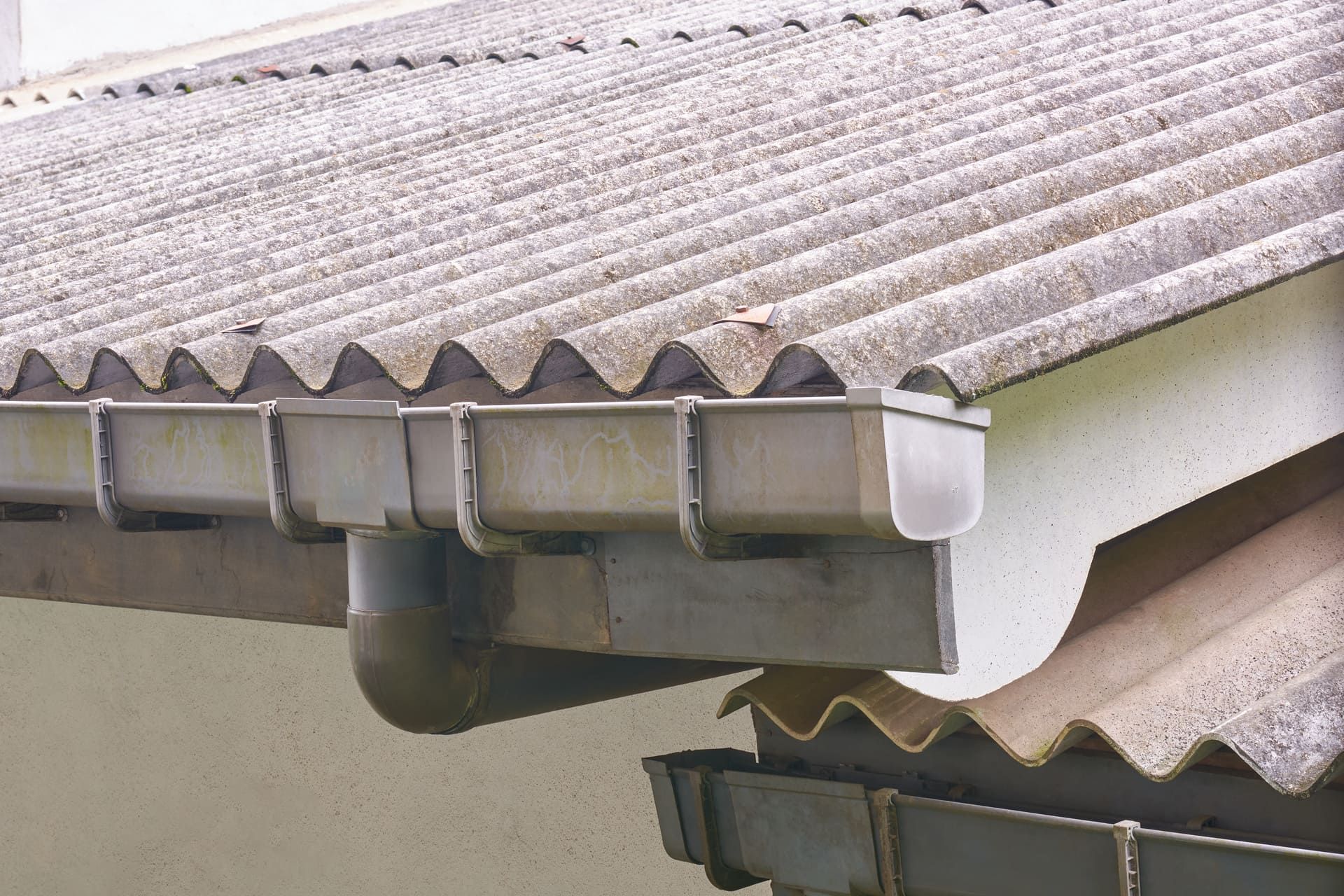 section of corrugated asbestos cement roof with attached plastic gutters and downspouts in close-up view, older structures of industrial or residential buildings
