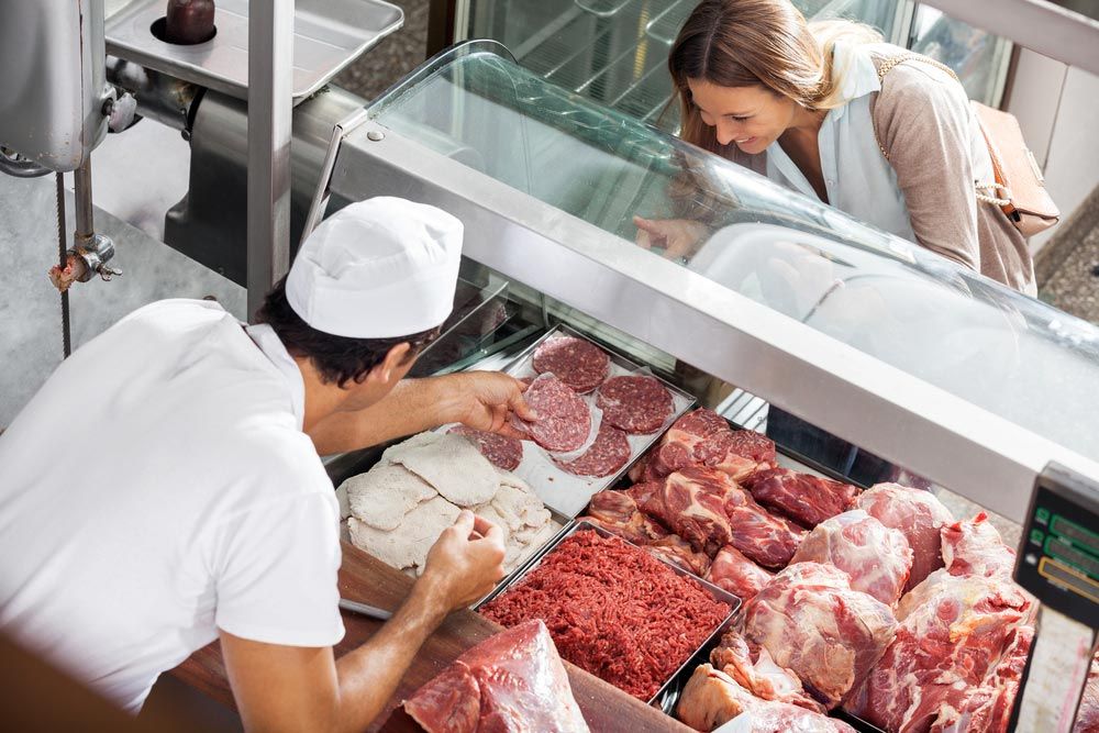 High Angle View Of Male Butcher Showing Meat To Female Customer — Quality Meats in Port Macquarie, NSW