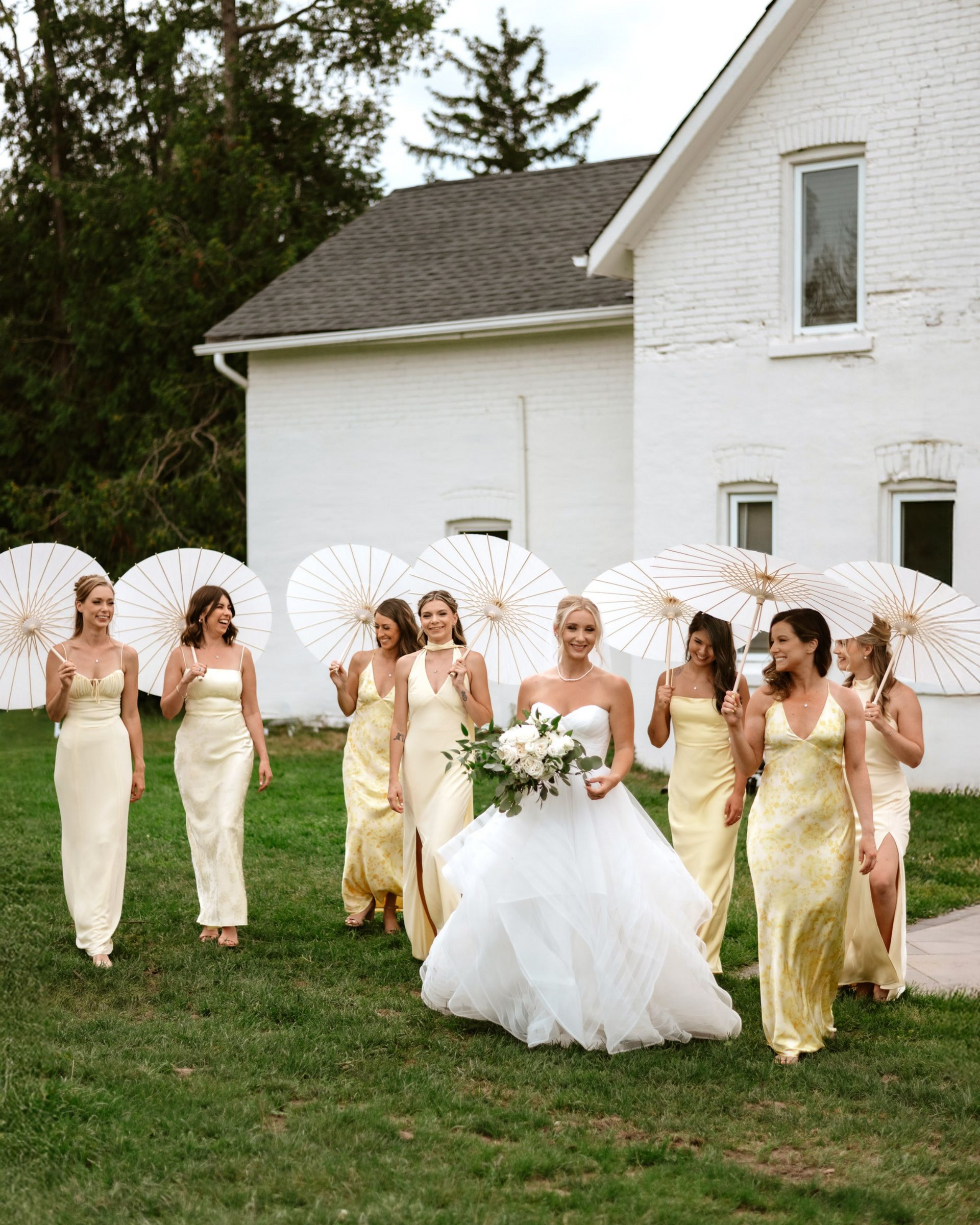 A bride in a white wedding gown walks on grass with bridesmaids in North Bay Ontario