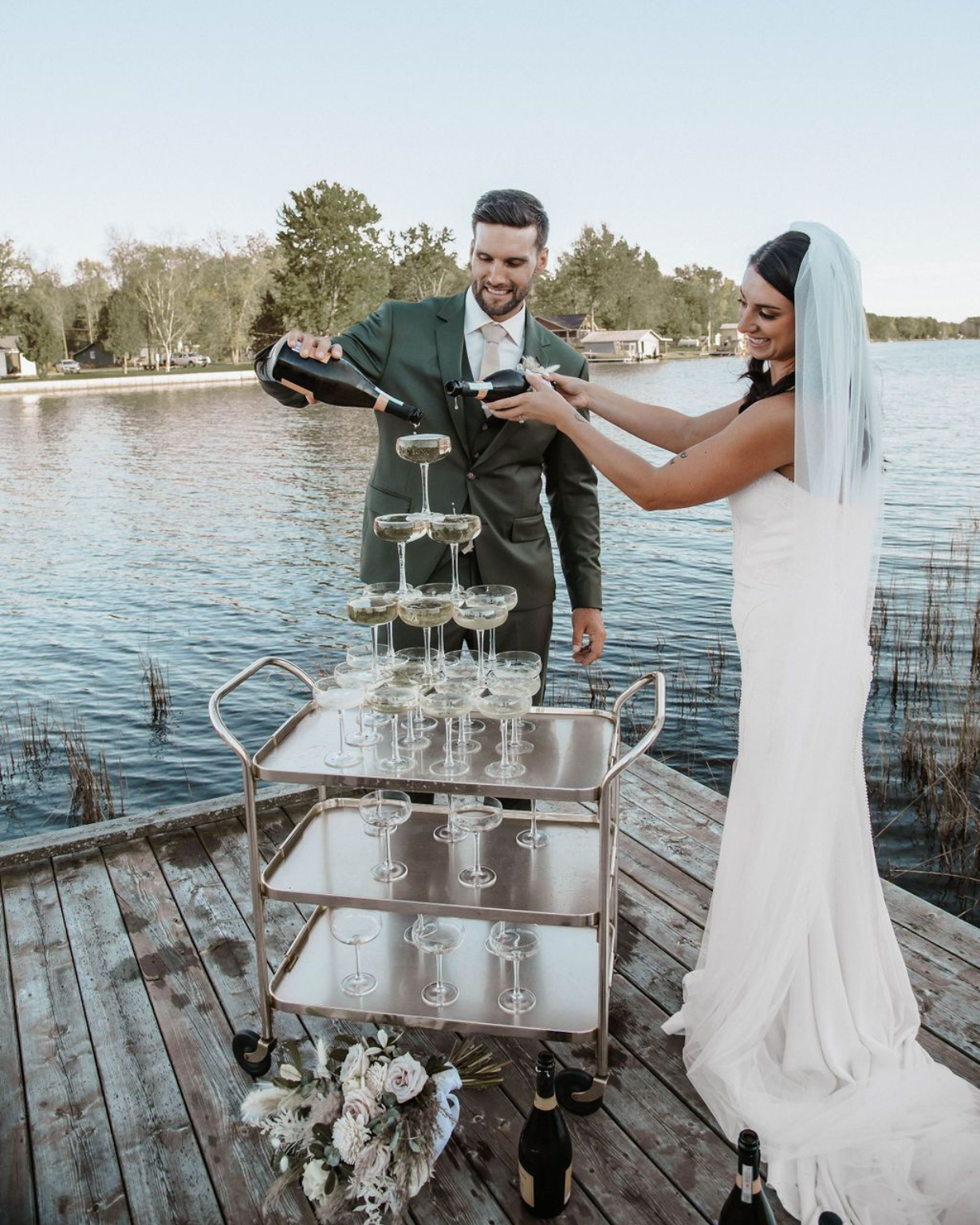 A bride and groom in wedding attire pour champagne into a stacked tower of glasses at a Dream wedding North Bay