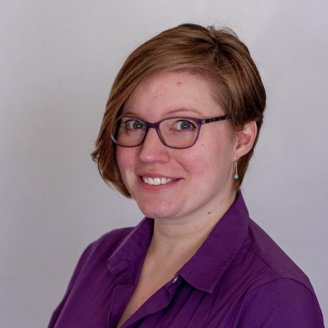 Picture of Stephanie Swilley. Female with glasses, smiling at the camera in front of a grey background.