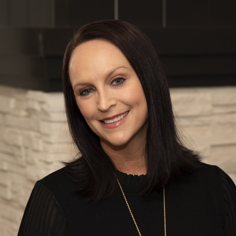 Picture of Katie Vigil. Female, smiling at the camera in front of a white brick background