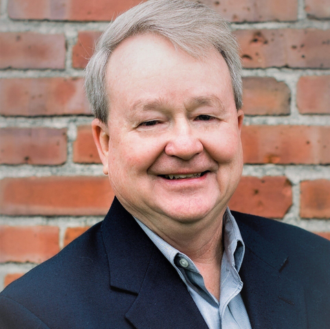 Picture of Tim Maupin. Male, smiling at the camera in front of a brick background