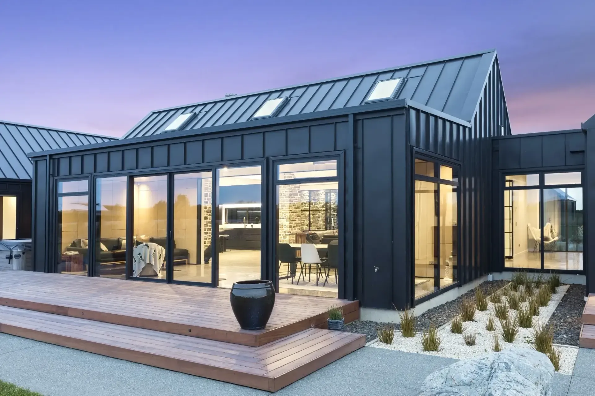 Modern black home with large windows, deck, and a gravel landscaping.