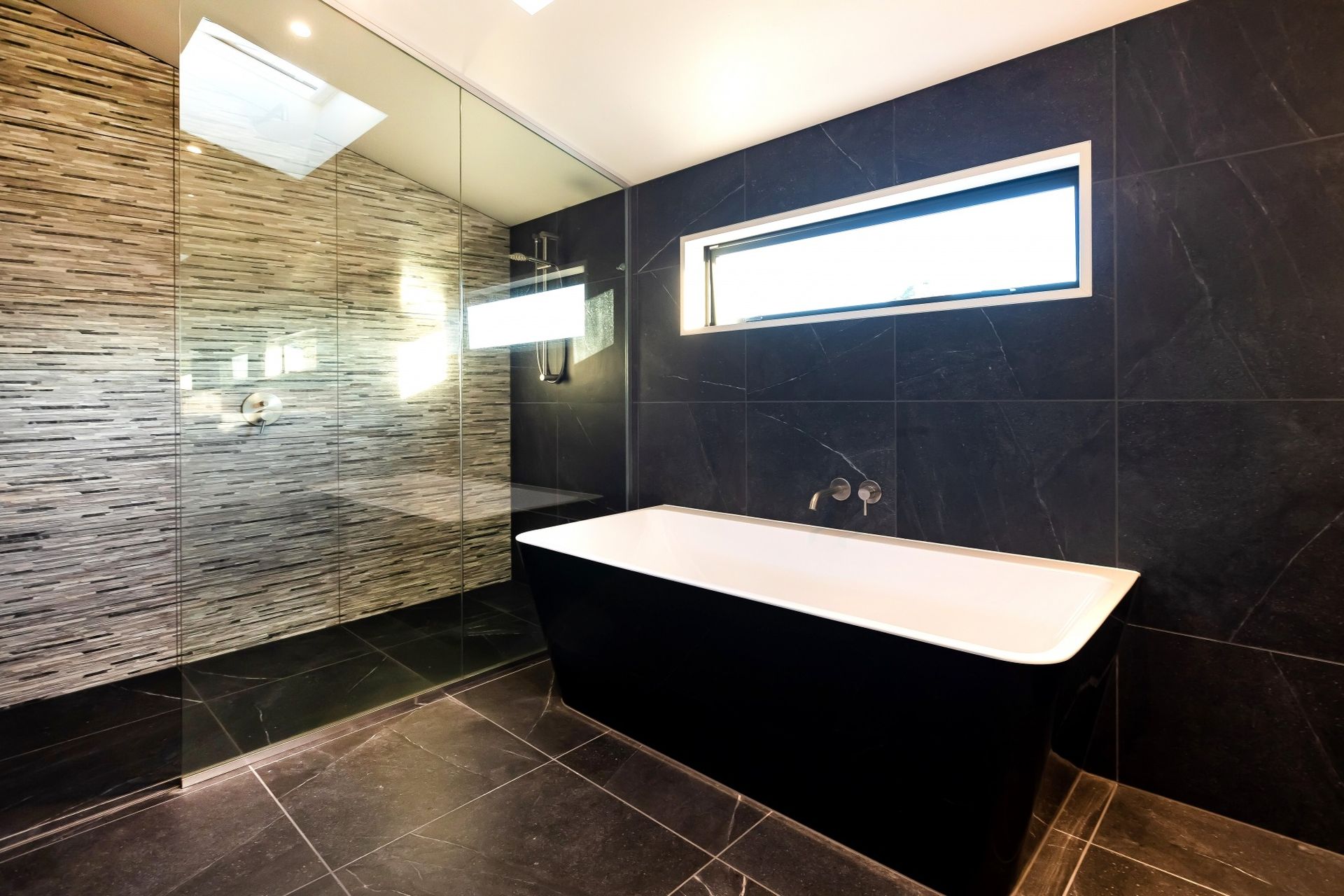Modern bathroom with black tile, walk-in shower, and a black and white tub.