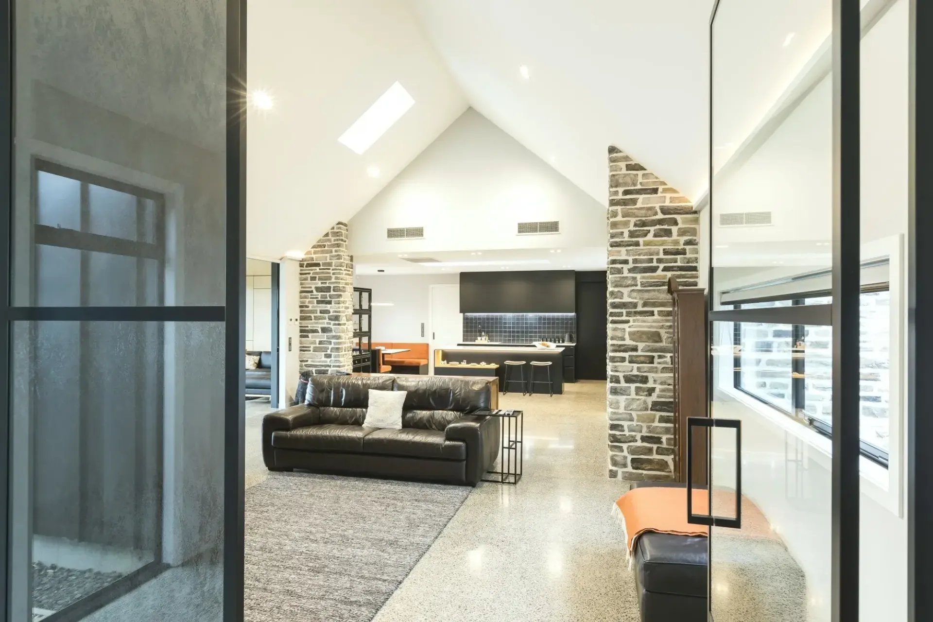Interior view of a modern living area with a leather sofa, stone accents, and a kitchen visible in the background.