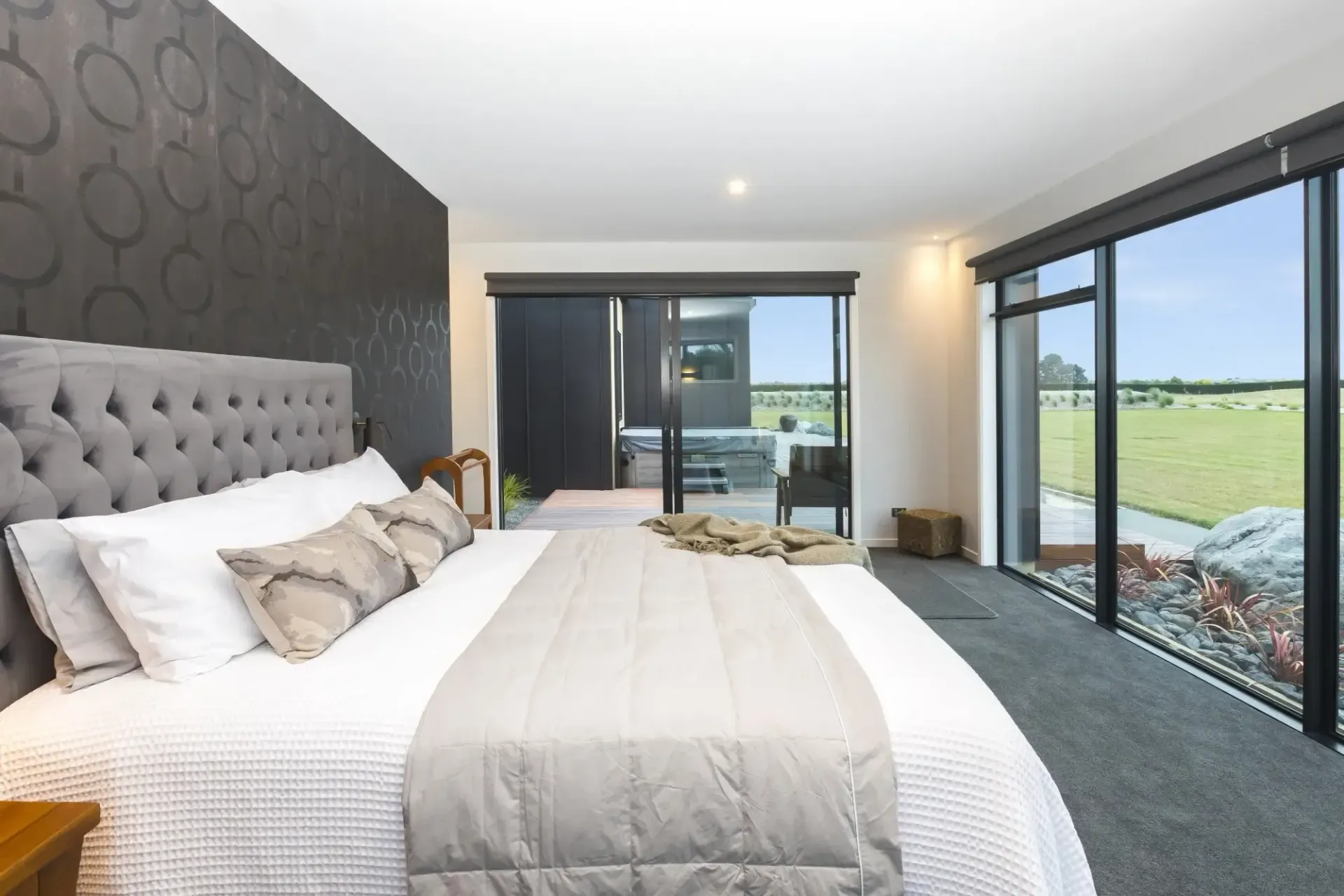 Bedroom with a large bed, tufted headboard, and sliding doors leading to a patio with a view of a field.
