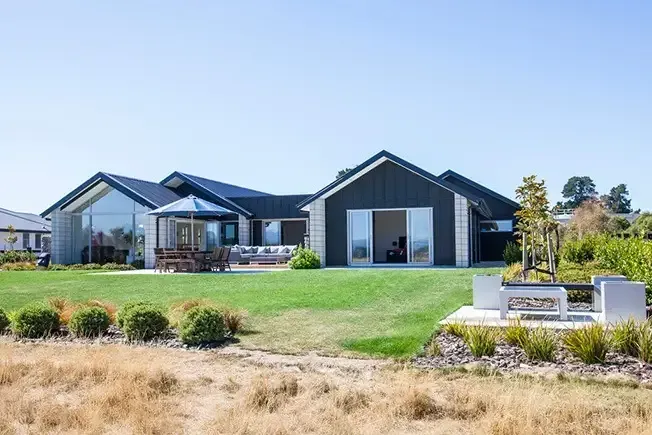 Modern black home with large windows and manicured lawn on a sunny day.