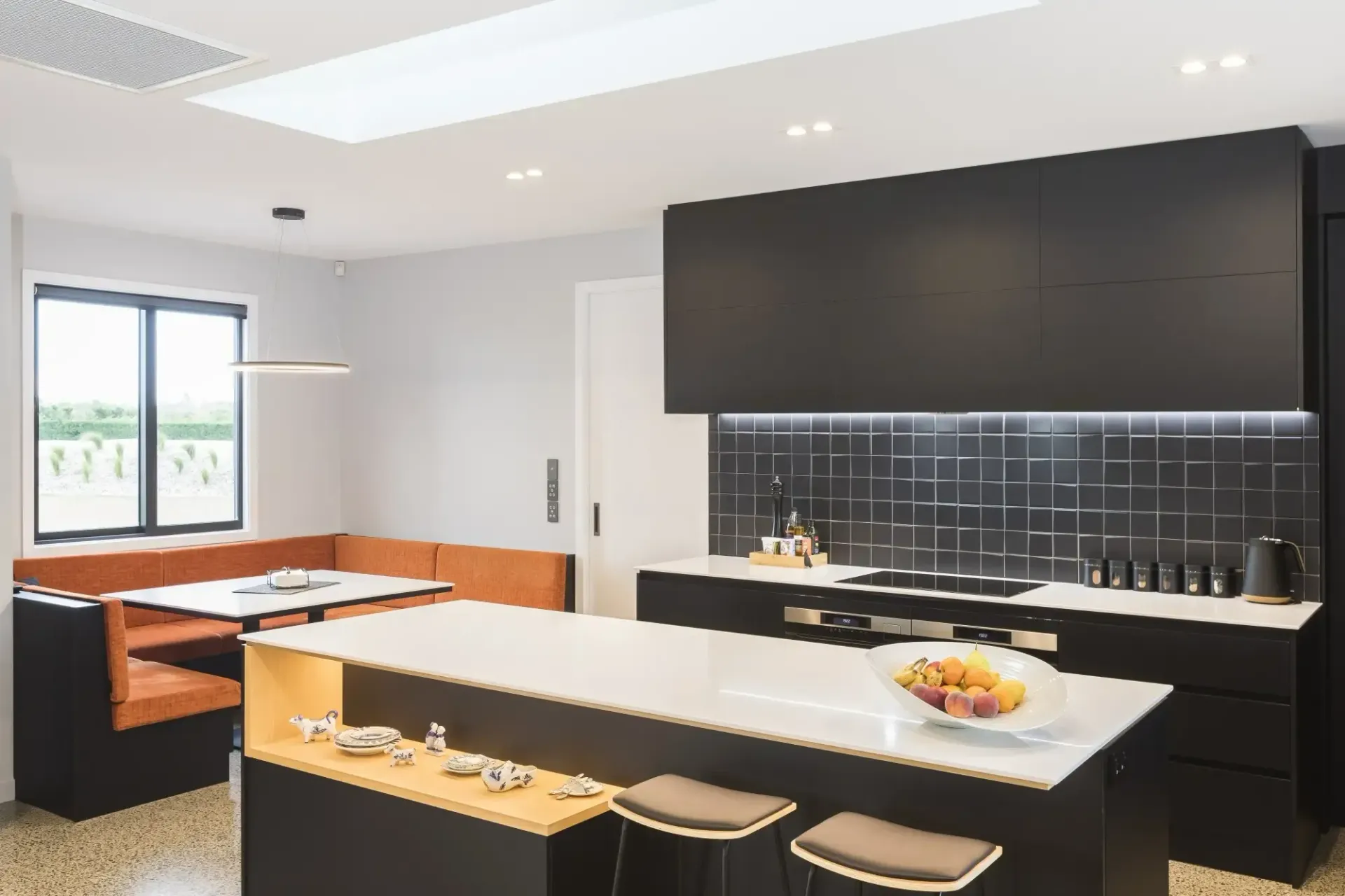 Modern kitchen with black cabinets, island, and orange booth seating.
