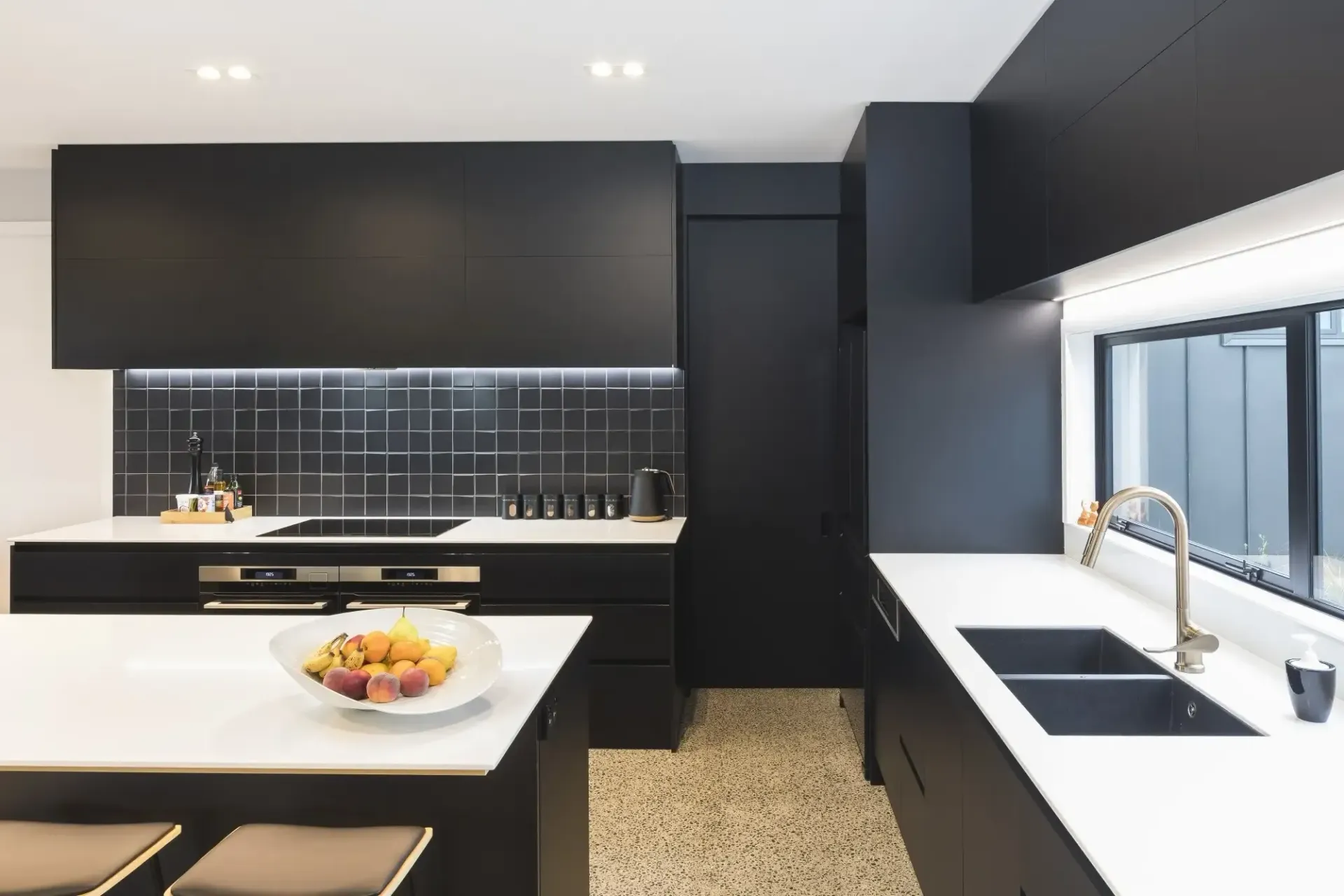Modern kitchen with black cabinets, white countertops, and a black backsplash.