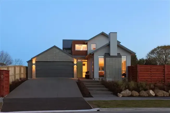 Modern house with gray exterior, driveway, and garage door. Wooden accents, chimney, and blue twilight sky.