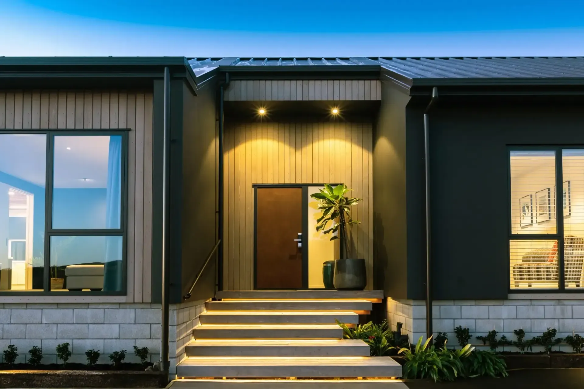 Modern home exterior with a dark door, steps, and windows at dusk.