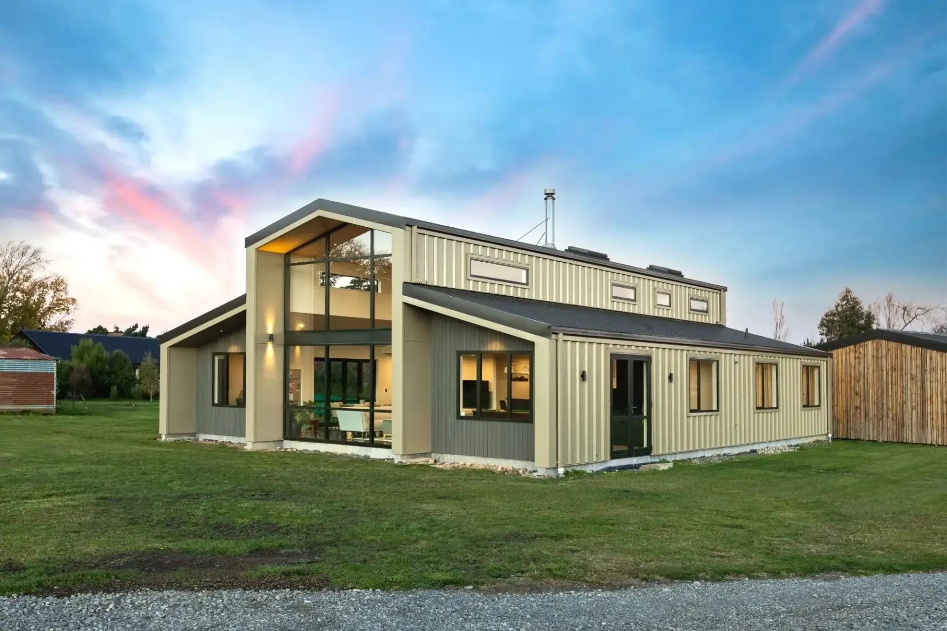 Modern house constructed from shipping containers, beige siding, glass windows, and green lawn.