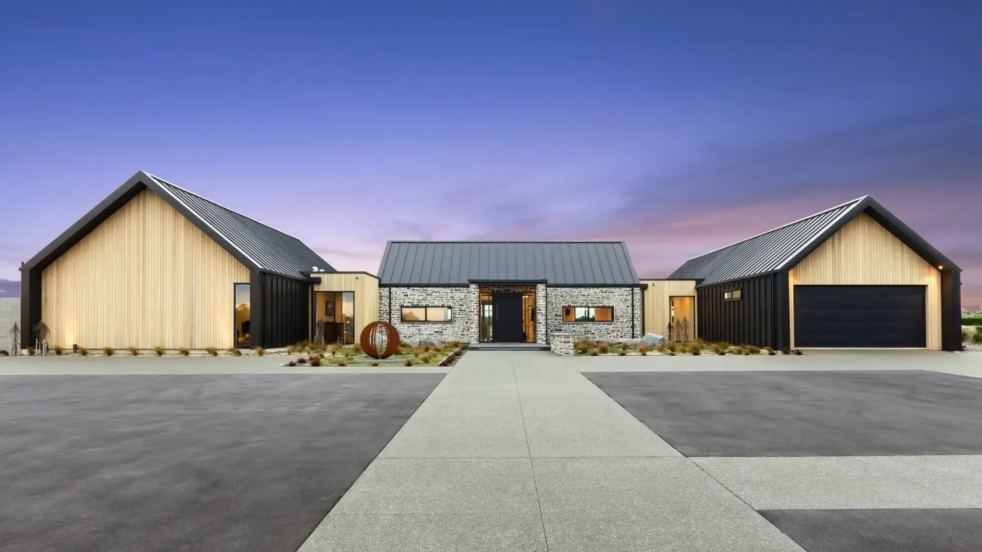 Modern home with wooden and stone facade under a twilight sky. Concrete path leads to the front entrance.