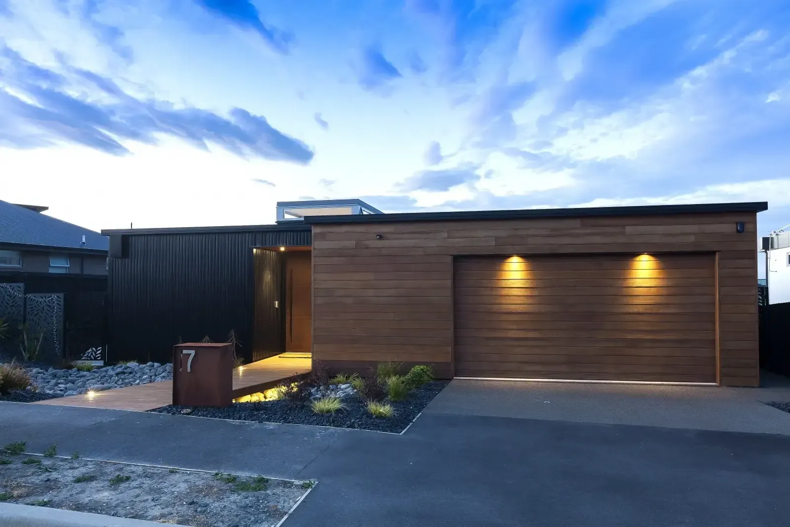 Modern house with wood siding and garage door, lit up at dusk.