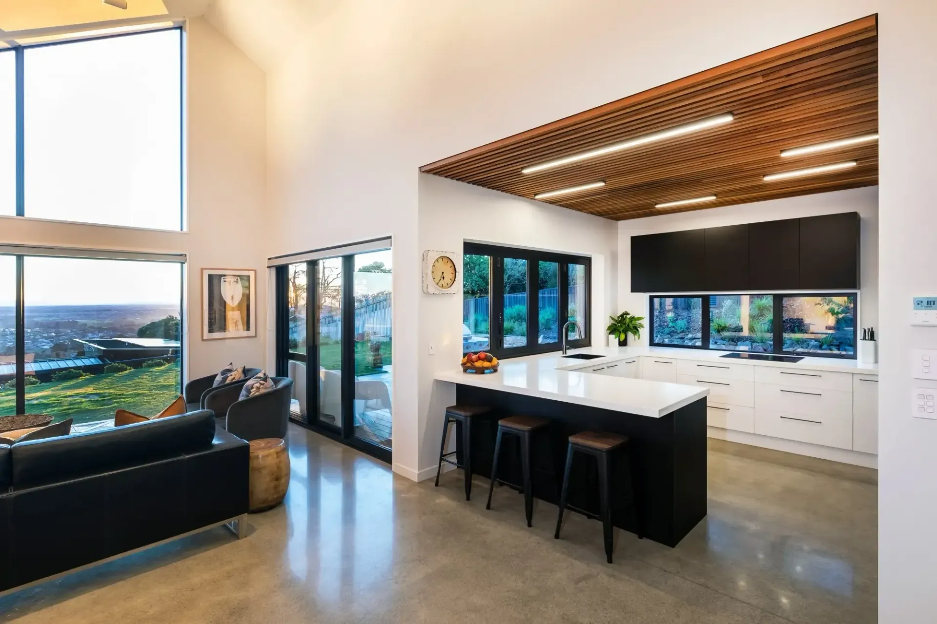 Modern kitchen and living area with black and white decor, large windows and scenic views.