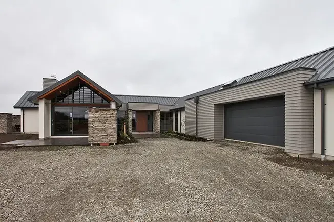 Modern home with gravel driveway, garage, and stone accents under a cloudy sky.