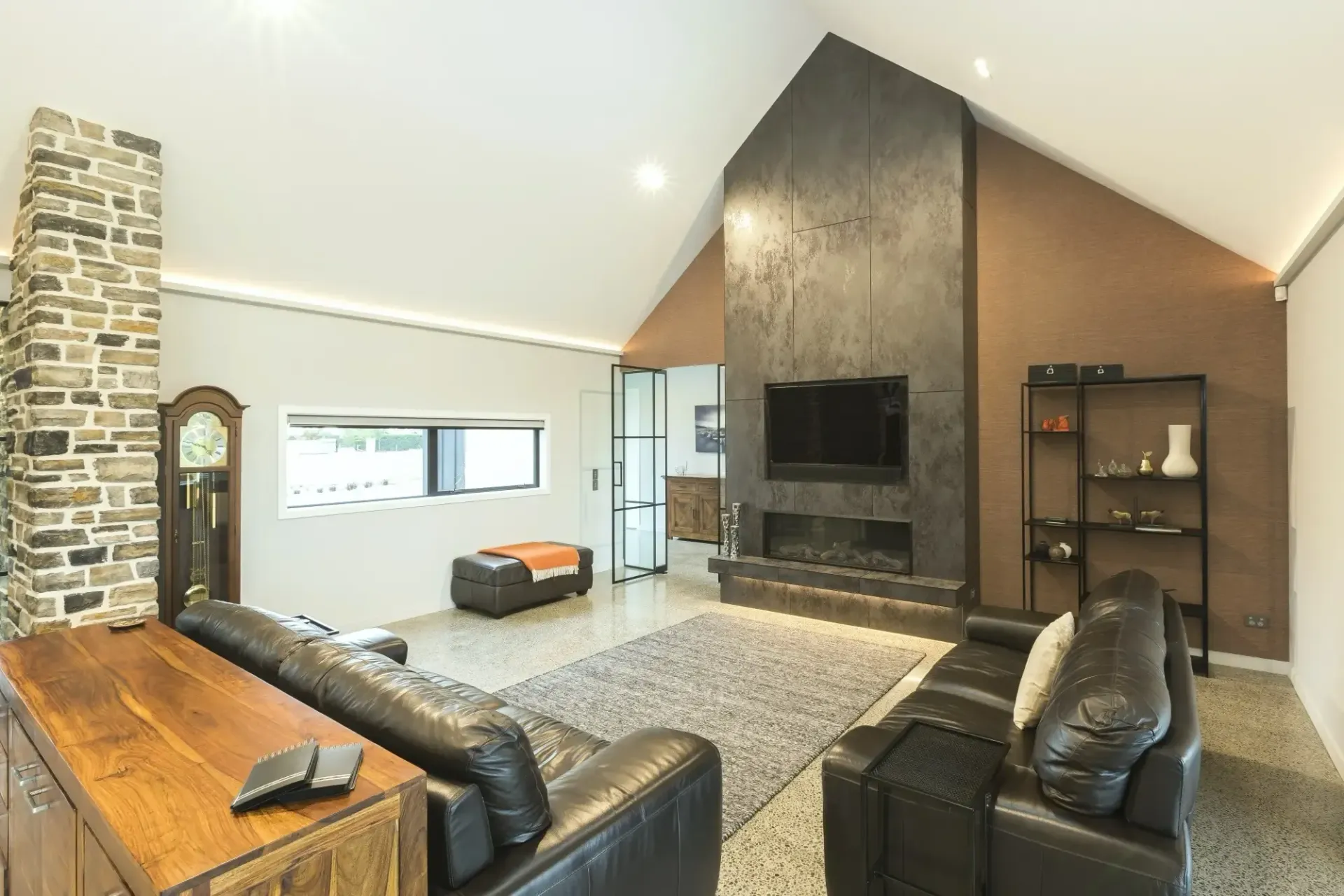 Living room with a stone column, dark leather sofas, fireplace, and a clock.