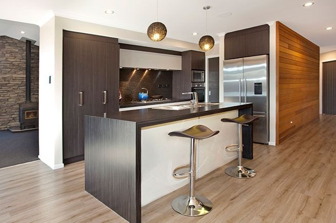 Modern kitchen with dark cabinets, island with stools, stainless steel appliances, and wood accent wall.